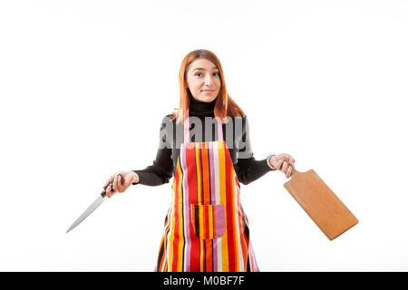 Eine junge rothaarige Frau in einem schwarzen Rollkragenpullover und Küche Schürze ist überrascht und hält ein großes Küchenmesser und eine Küche aus Holz Board für das Schneiden von o Stockfoto