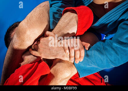 Mann Ringkämpfer der Auseinandersetzung und Jiu jitsu in blauen und roten Kimono macht Submission wrestling Kampftechniken: armbar armlock, Stockfoto