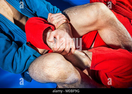 Close-up zwei Ringkämpfer der Auseinandersetzung und Jiu jitsu in blauen und roten Kimono macht armbar. Submission wrestling auf Blau tatami Stockfoto