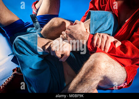 Zwei Ringkämpfer der Auseinandersetzung und Jiu jitsu in blauen und roten Kimono macht armlock auf Blau Tatami. Close-up Wrestler submission wrestling Stockfoto