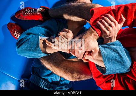 Close-up zwei ringkämpfer von sambo und Jiu jitsu in blauen und roten Kimono zu tun. Man Wrestler macht Submission wrestling oder armbar auf Blau tatami Stockfoto