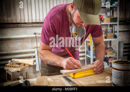 Ein junger Mann builder Zimmermann arbeitet mit einer Bar aus Holz für Möbel, Maßnahmen und Schnitte in der Werkstatt, im Hintergrund von vielen Tools Stockfoto