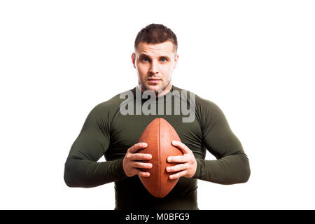 Eine junge Dunkelhaarige männlichen Wrestler in einem grünen Sport rashgard lächelt und hält einen Rugby Ball in den Händen von einem weißen Hintergrund isoliert Stockfoto