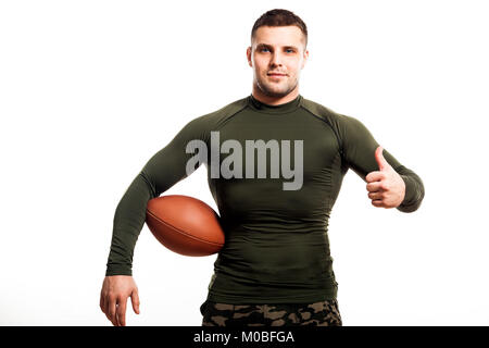 Junge dunkelhaarige Mann Wrestler in grün Sport rashgard lächelnd, mit einem rugby ball und Daumen hoch, gegen Weiße isoliert Hintergrund Stockfoto