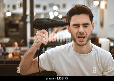 Junge verrückt stilvollen Mann mit Fön und lustige Ausdrücke im barbershop. Stockfoto