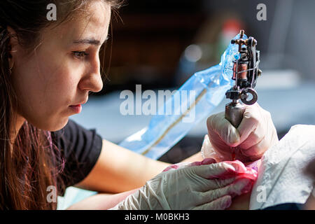 Junge dunkelhaarige Frau tattoo Master, Tattoo von einem kleinen Vogel mit rot Tattoo Maschine, close-up Stockfoto