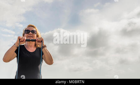 Model Released: reife Frau (70-75) Training mit einem Stück Schnur gegen den blauen Himmel Platz kopieren Stockfoto