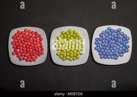 Drei Platten mit bunten Bonbons Pralinen mit RGB-Farben auf schwarzem Hintergrund Stockfoto