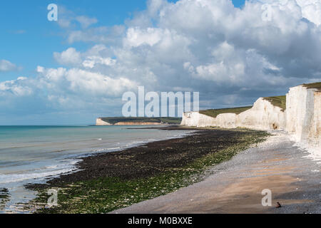 Birling Gap in der Nähe von Beachy Head Sussex. Sieben Schwestern Kreidefelsen mit Sturmwolken über Rollen. Ruhiges Meer mit eingehenden Flut auf Pebble Beach. Sonnigen Tag Stockfoto