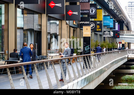 London, Großbritannien - 25 November 2017 - Ein Geschäftsmann bei Crossrail in Canary Wharf mit Restaurants und Geschäften im Hintergrund Stockfoto