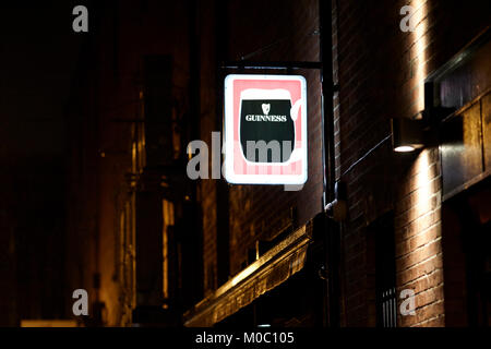 Alte beleuchtete Guinness Schild an der Wand von einer Kneipe in einer feuchten regnerischen Nacht in Belfast Nordirland UK Stockfoto