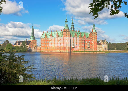 Das Schloss Frederiksborg im holländischen Renaissance-Stil in Hillerød, Nordsealand, Dänemark, bei strahlendem Sonnenschein am Sommermorgen, der durch die Frühlingsblätter gesehen wird. Stockfoto