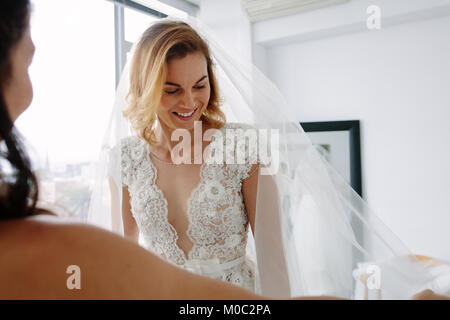 Schöne junge Frau, die versucht, auf Hochzeit Kleid in bridal Shop mit Assistant. Zukünftige Braut die Montage der neuen Kleid in Hochzeit Mode Shop. Stockfoto