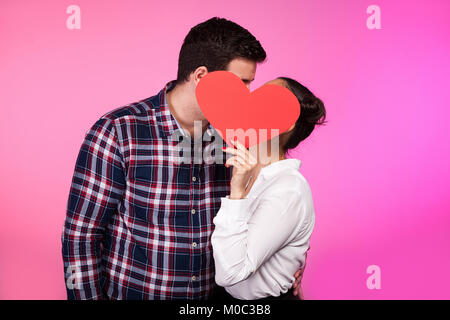 Paar hinter einem Herzen aus Pappe küssen Stockfoto