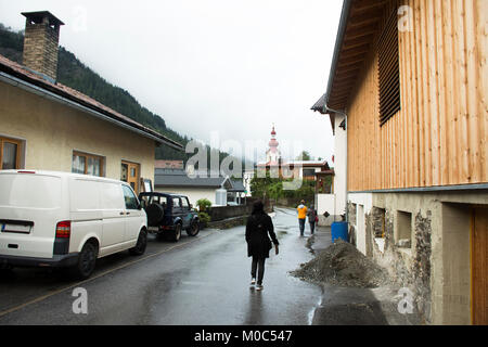 Reisende Menschen zu Fuß in kleinen Gasse gehen Sie zu Kath Pfarramt Kirche in Pfunds Dorf, während abends Zeit und Regen am 2. September 2017 in Tirol, Österreich Stockfoto
