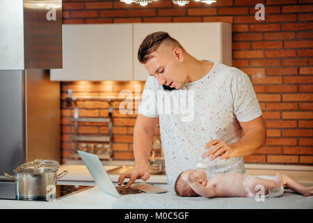 Vater Fütterung sein Baby beim Arbeiten am Laptop Stockfoto