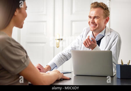 Junge fröhliche cosmetologist Mann an einem Laptop im Büro zu sitzen und die Kommunikation mit der Frau. Stockfoto