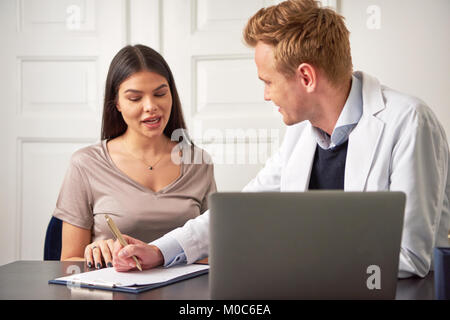 Kosmetiker Mann am Laptop im Büro zu sitzen und eine Beratung für die Frau, die während der Arbeit mit Papieren. Stockfoto