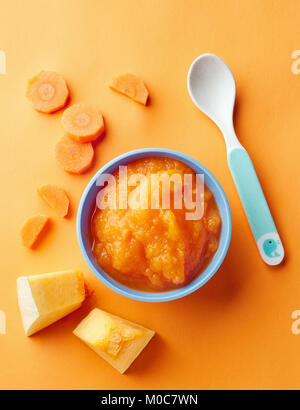 Kürbis und Karotte Baby pürieren in Schüssel mit Baby Löffel auf orangem Hintergrund, Ansicht von oben Stockfoto