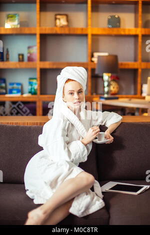 Junge Frau im Bademantel Kaffee trinken und Lesen auf digital Tablet Stockfoto