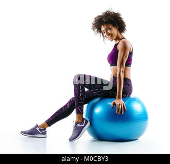 Lächelnde Mädchen ruht auf Gymnastikball. Foto von sportlichen afrikanisches Mädchen in Sportkleidung auf weißem Hintergrund. Sport Stockfoto