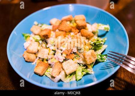 Makro Nahaufnahme von hausgemachten Ceasar Salat auf blauen Platte, Holztisch, Gabel, Croutons, Salat Stockfoto