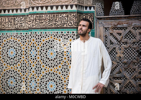 Arabischer Mann in traditioneller Kleidung, langen weißen Hemd vor der Wand mit Text aus dem Koran Stockfoto