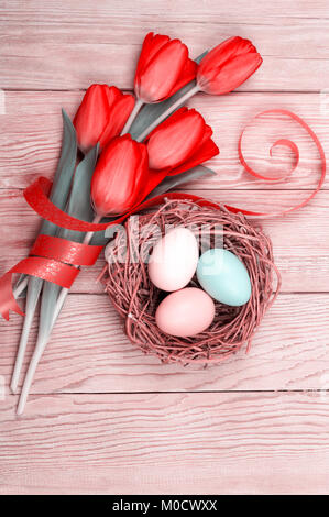 Easter Eggs in ein Vogelnest mit bunten Tulpen auf hölzernen Hintergrund Stockfoto