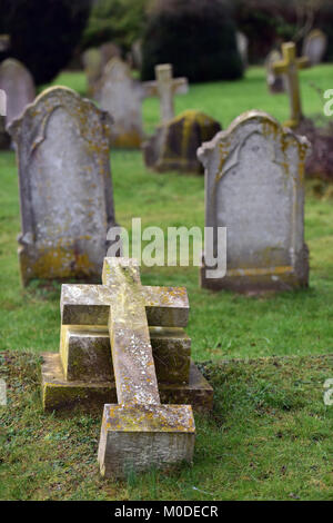 Eine gefallene Kreuz auf einem Friedhof mit Gedenkstätte Grundsteine im Hintergrund. Ein Friedhof mit einem gebrochenen religiösen Kreuz oder Symbole zerstört oder beschädigt. Stockfoto