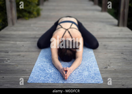 Frau Yoga auf einer Matte auf einen Holzsteg, der Bein Kind darstellen. Konzentrieren Sie sich auf die Hände. Stockfoto