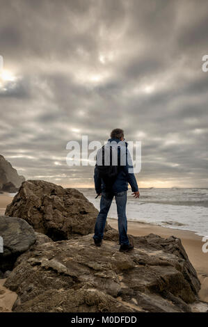 Mann mit einem Rucksack auf Felsen über dem Meer. Stockfoto