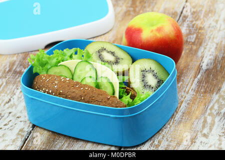 Gesundes Lunchpaket mit braunen Käse Sandwich, Kiwi und roter Apfel auf Holzmöbeln im Landhausstil Oberfläche Stockfoto