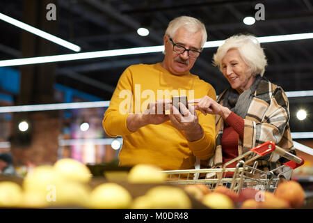 Senioren mit Smartphone im Supermarkt Stockfoto