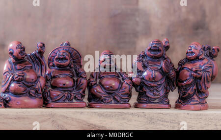 Eine Reihe von fünf Lachen, Happy Buddha Ornamenten, mit sichtbaren fetten Bäuchen, angezeigt im Innenraum in einem Holzschrank auf einem Regal. England, UK. Stockfoto