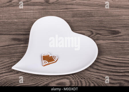 Valentinstag Herzen für gutes Glück, Hand-verzierte Lebkuchen und weiße Platte. Symbole der Liebe, Bond, Ehe oder Freundschaft auf braunem Holz Hintergrund. Stockfoto