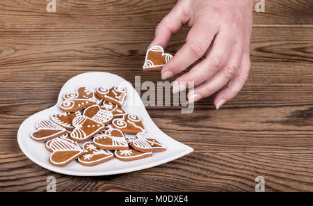 Weibliche Hand, die eine schöne süße Herz für Glück und weiße Platte. Symbole der Liebe, Bond, Ehe oder Freundschaft auf braunem Holz Hintergrund. Stockfoto