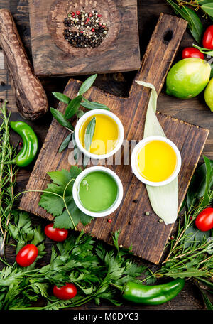 Öle, Gewürze und Kräuter. Trauben, Oliven und Mais Öle frische Kräuter Zitronen, Paprika. Ansicht von oben. Stockfoto