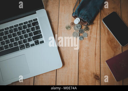 Die Thailändische und Hong Kong Münzen in blauen Stoff Tasche auf Holz Tisch neben Notebook und Handy. Stockfoto