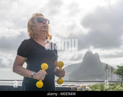 Reife Frau (70-79) Training mit Kurzhanteln an öffentlichen Turnhalle in Ipanema, Rio de Janeiro, Brasilien Stockfoto