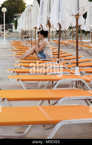 Frau sitzt auf einem Liegestuhl am Strand Stockfoto