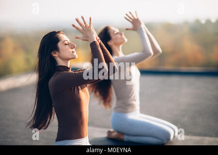 Zwei junge schöne Frauen Yoga Asana, sitzen in Vajrasana Übung auf dem Dach im Freien. Die Freundinnen führen Sie eine bequeme Haltung der östlichen pract Stockfoto