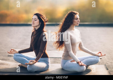 Zwei junge Frauen, die Meditation im Lotussitz auf dem Dach im Freien. Padmasana Stockfoto