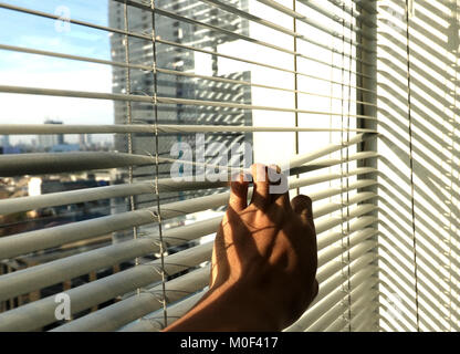 Hand, denn ein Blick durch das Fenster Jalousien Stockfoto