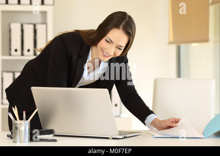 Happy Büroangestellter arbeiten Vergleichen von Dokumenten auf Linie mit einem Laptop Stockfoto