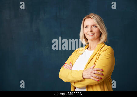 Close-up Studio Aufnahme einer wunderschöne reife Frau, die mit verschränkten Armen an dunklen bacgkround. Stockfoto