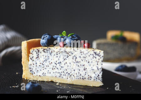 Käsekuchen mit Mohn, Blaubeeren und minzeblatt auf dunklen Schneidebrett. Detailansicht. Getonten Bild Stockfoto