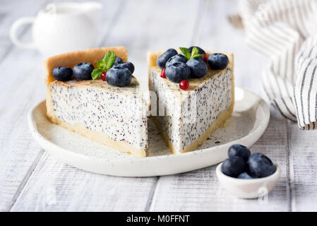 Käsekuchen mit Mohn und Heidelbeeren. Hausgemachte Mohn Torte auf weißen Teller dekoriert mit Blaubeeren und Minze. Detailansicht Stockfoto