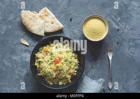 Tabbouleh mit Cous Cous und arabisch Fladenbrot auf konkreten Hintergrund. Gesunde diätetische Mahlzeit. Tabelle Ansicht von oben Stockfoto