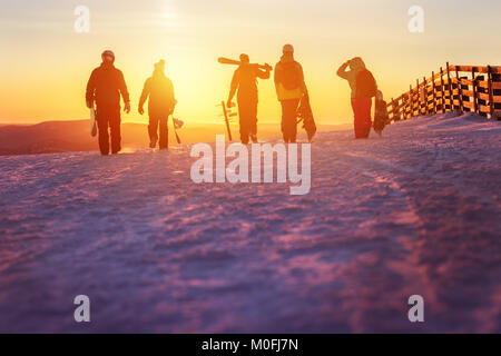 Freunde mit Ski und Snowboards zu Fuss bis Sonnenuntergang Stockfoto