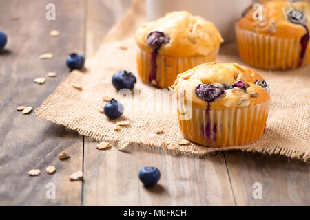 Frisch gebackene blueberry muffins mit Mandel-, Hafer und Puderzucker Topping auf einem rustikalen Holztisch mit Beeren Stockfoto